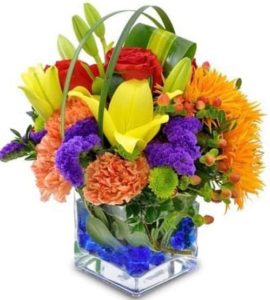 Exhilarating colors of Gerbera Daisies, lilies, roses, carnations, statice and more create a festive feeling with this bold cube-vase floral gift. Perfect for a desk, home or any occasion.