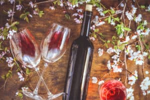 a bottle of wine, glasses with red wine and flowering branch of fruit tree, on a wooden background